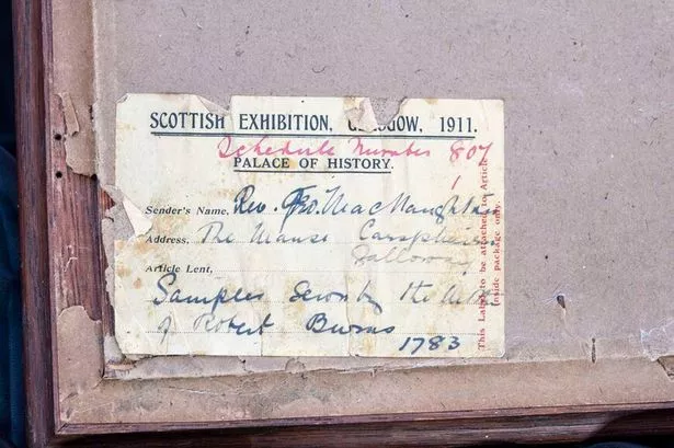 Close-up detail of faded handwritten labels on backs of the embroidery frames showing their connection to Dumfries and Galloway